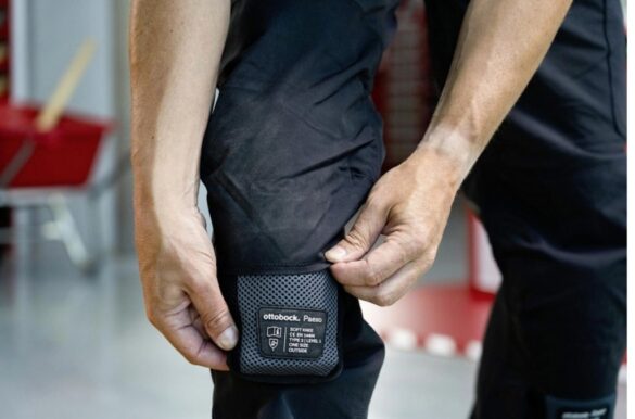 Personne ajustant une genouillère noire Ottobock Paexo, partie d’un exosquelette de protection utilisé pour le travail au sol.